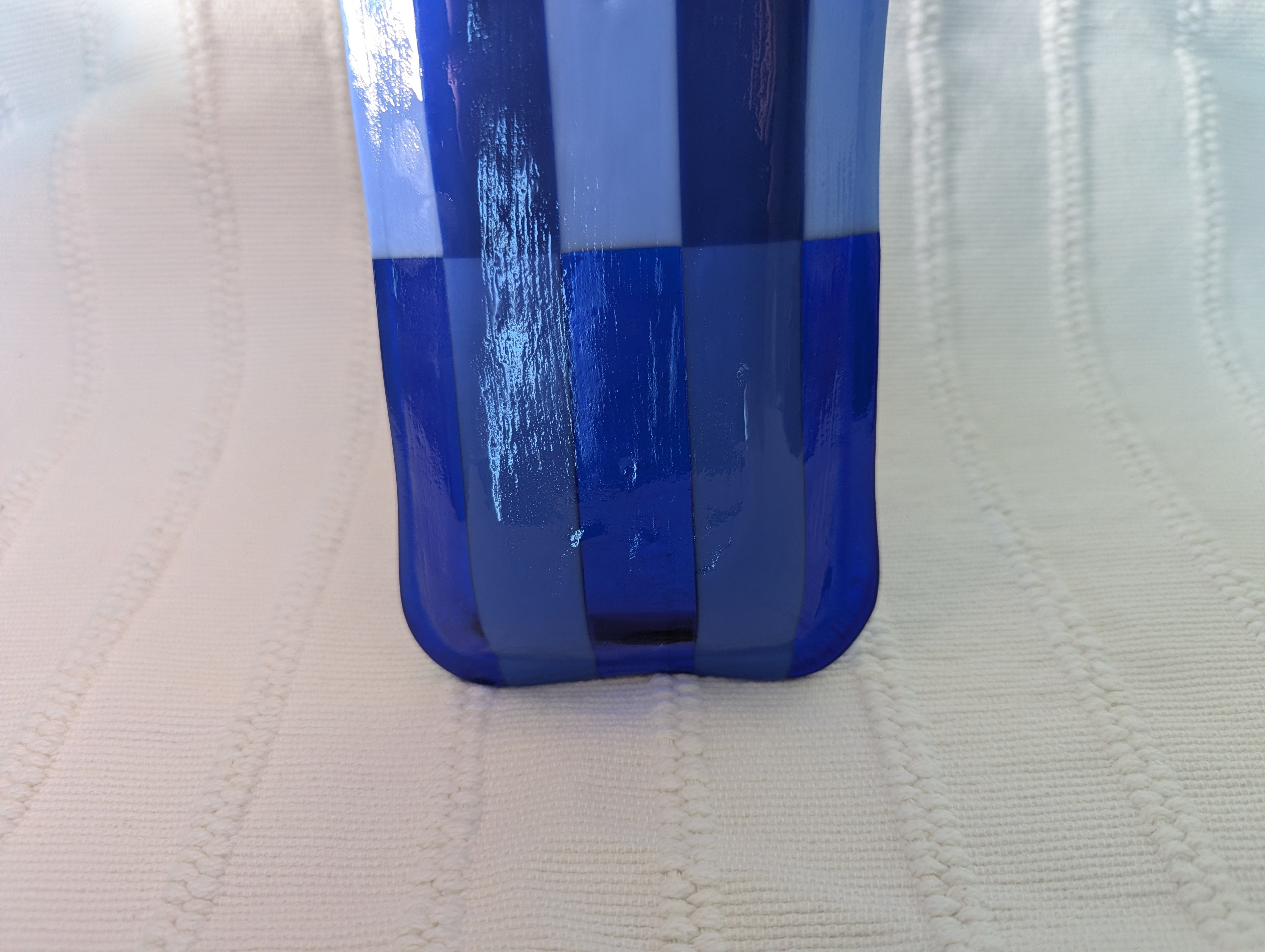 A close-up of a blue and white checkered glass tray on a textured off-white fabric background.