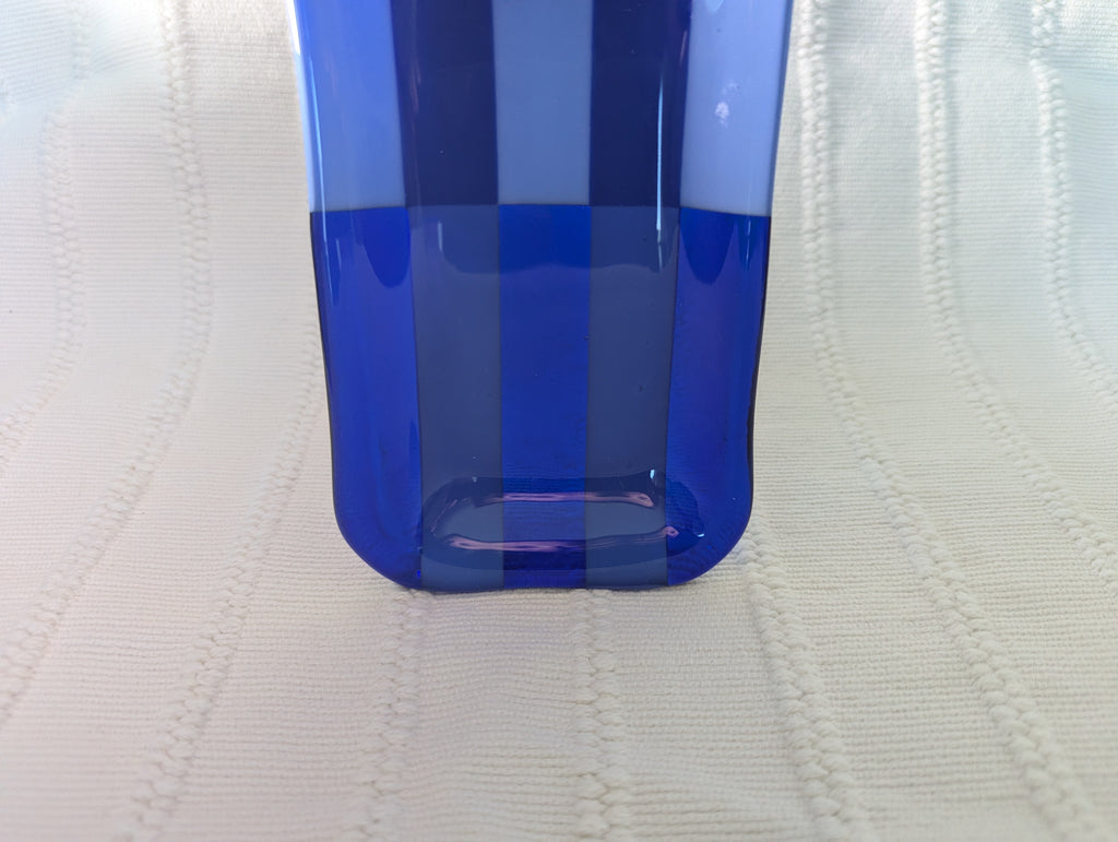 A close-up of a translucent blue glass tray with a rounded bottom, standing on a textured off-white fabric background.