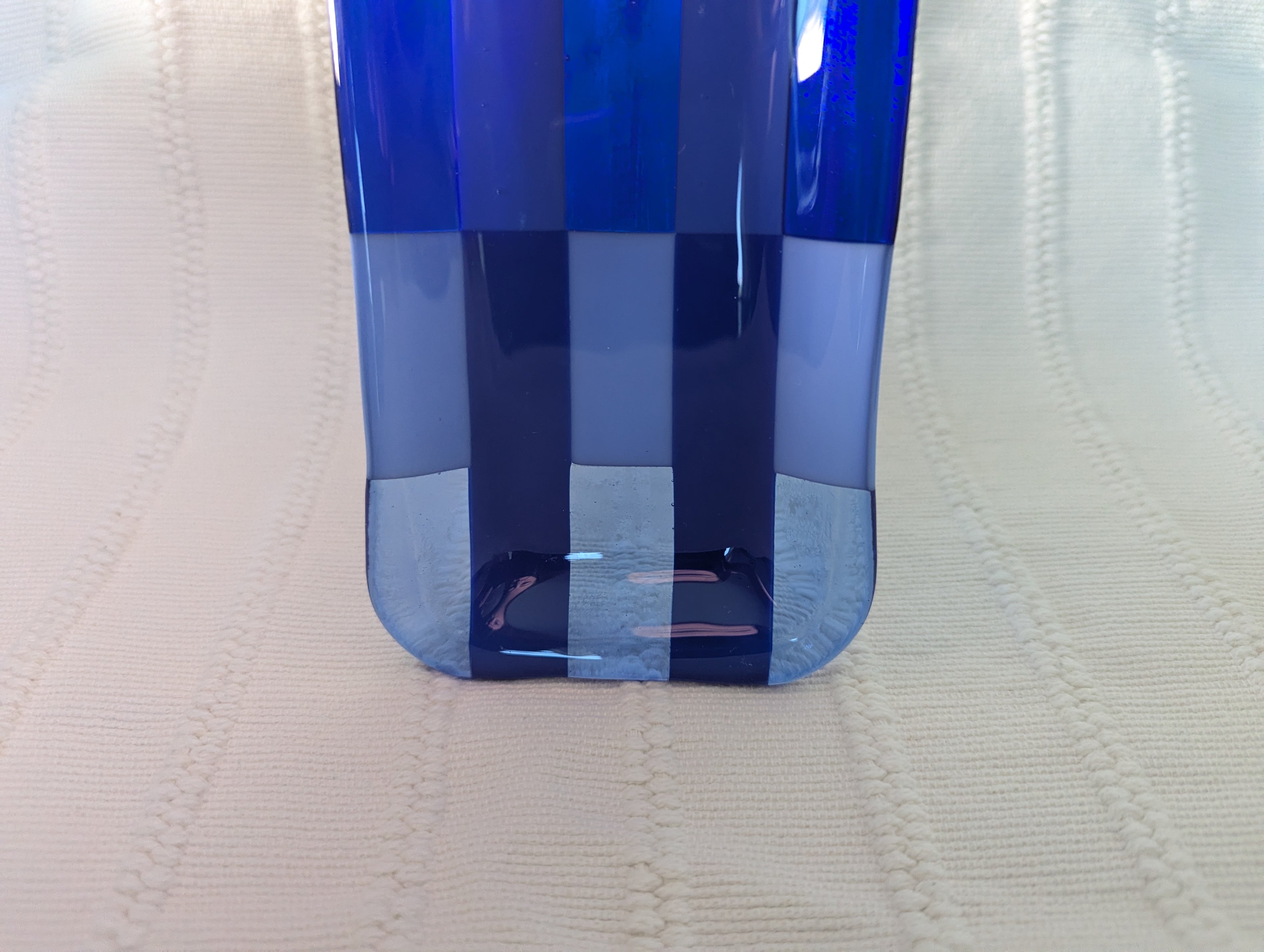 A close-up of a translucent blue glass tray with a rounded bottom, standing on a textured off-white fabric background.